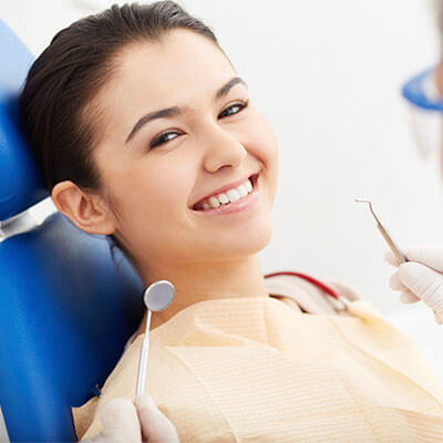 A young woman smiling while sitting in the blue chair of the Palms dentist