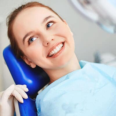 A teenage redhead in the Palms Dentistry dental office, lying in the dentist's blue chair while smiling and looking at one of our dental assistants