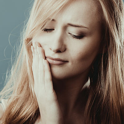 Our TMJ services showing a long-haired young woman with jaw pain while placing her hand on her cheek