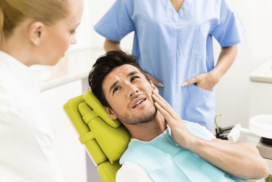 A male patient sits in the dentist's chair and indicates his pain